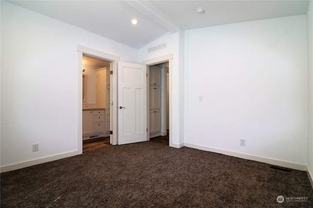 unfurnished bedroom featuring ensuite bath, vaulted ceiling with beams, and dark colored carpet