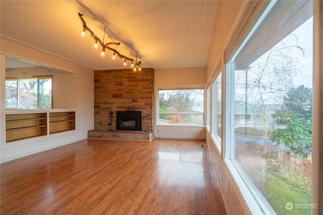 unfurnished living room featuring a stone fireplace, hardwood / wood-style floors, a wealth of natural light, and rail lighting