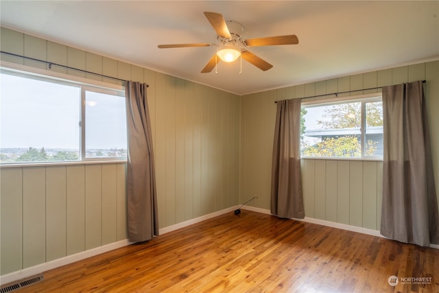 spare room with wood walls, ceiling fan, and light hardwood / wood-style flooring