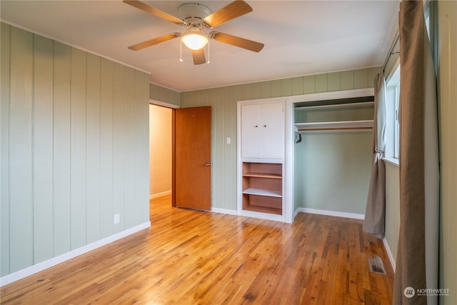 unfurnished bedroom with light wood-type flooring, wood walls, ceiling fan, and a closet