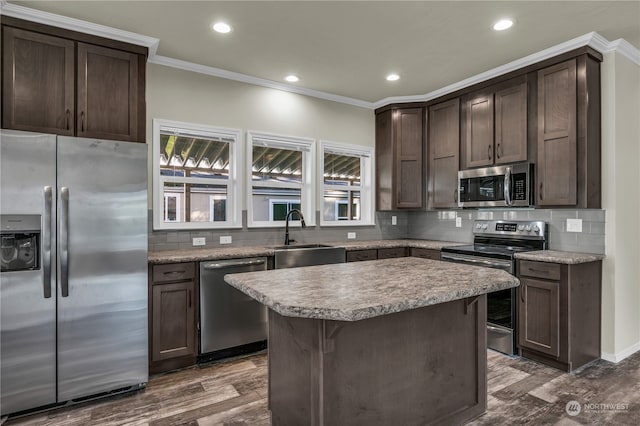 kitchen featuring appliances with stainless steel finishes, sink, a center island, dark wood-type flooring, and ornamental molding