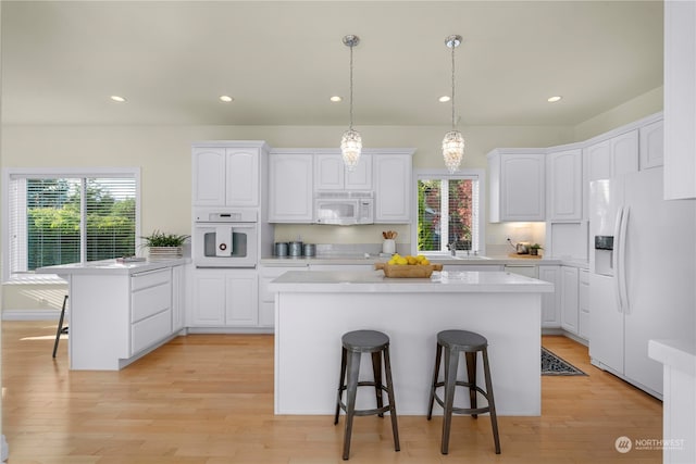 kitchen with a kitchen island, a breakfast bar area, light hardwood / wood-style flooring, white cabinets, and white appliances