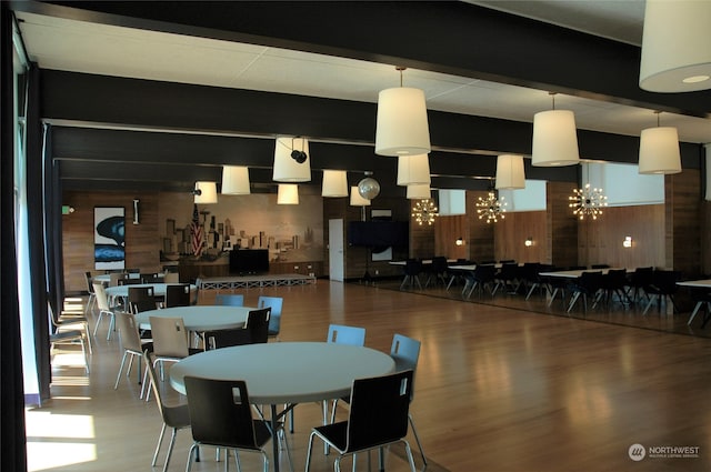 dining space featuring beamed ceiling, a chandelier, hardwood / wood-style flooring, and wooden walls