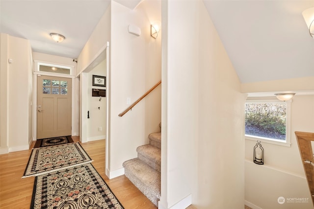 foyer entrance featuring light wood-style floors, vaulted ceiling, baseboards, and stairs