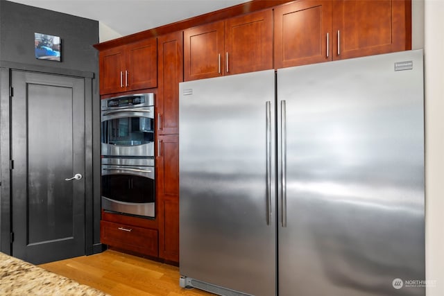 kitchen with light stone countertops, appliances with stainless steel finishes, and light hardwood / wood-style flooring