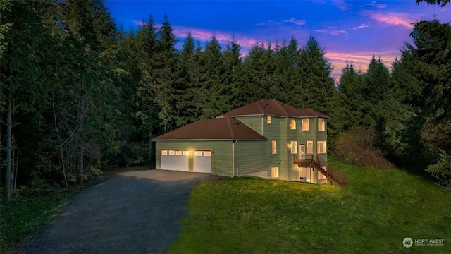 view of front of house featuring aphalt driveway, a yard, stairway, a wooded view, and a garage