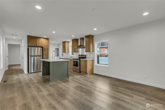 kitchen featuring a kitchen island, appliances with stainless steel finishes, light wood-type flooring, wall chimney exhaust hood, and sink