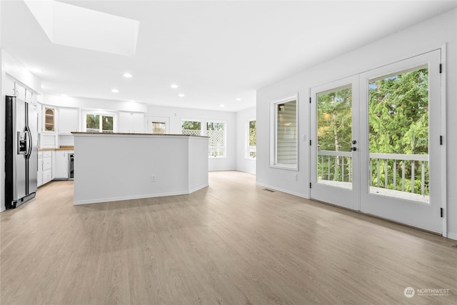 unfurnished living room featuring french doors, light hardwood / wood-style floors, and a skylight