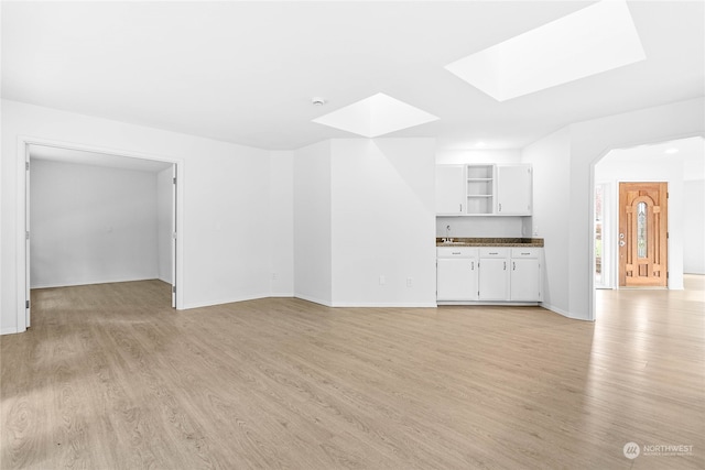 unfurnished living room with light hardwood / wood-style floors, sink, and a skylight