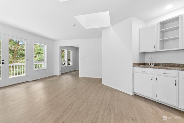 kitchen featuring white cabinetry, sink, light wood-type flooring, and a skylight