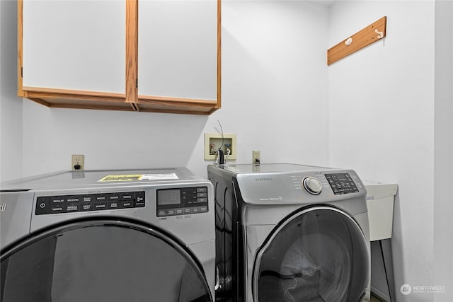 clothes washing area with washer and clothes dryer and cabinets