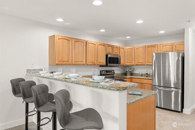 kitchen with stainless steel appliances, kitchen peninsula, light tile patterned floors, a breakfast bar area, and light stone countertops