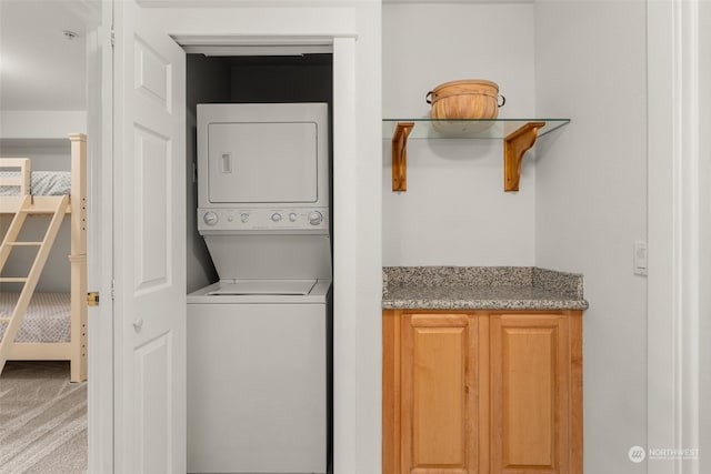 clothes washing area featuring stacked washer and clothes dryer and carpet