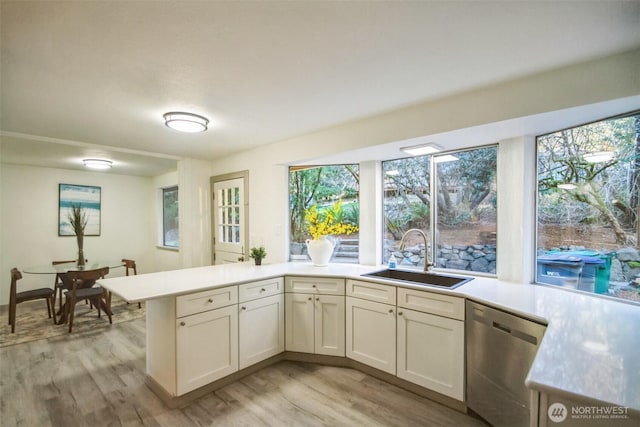 kitchen with dishwasher, light countertops, a peninsula, and a sink