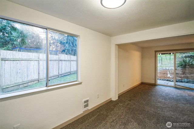 empty room with dark colored carpet, baseboards, and a textured ceiling