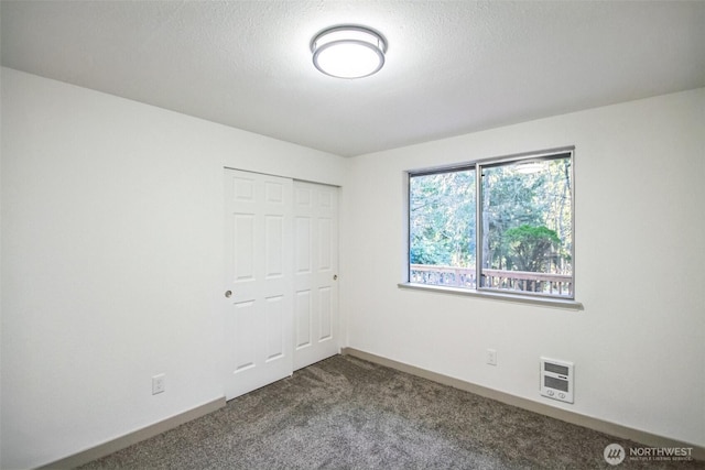 unfurnished bedroom featuring baseboards, heating unit, carpet flooring, a closet, and a textured ceiling