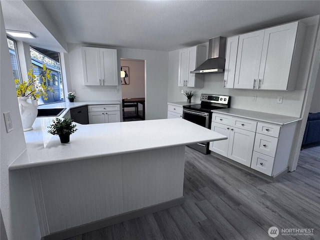 kitchen featuring dark wood-type flooring, stainless steel range with electric stovetop, white cabinetry, wall chimney exhaust hood, and light countertops