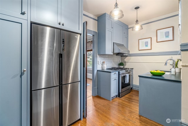 kitchen featuring appliances with stainless steel finishes, backsplash, hanging light fixtures, ventilation hood, and light wood-type flooring