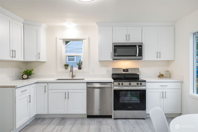 kitchen with appliances with stainless steel finishes, a healthy amount of sunlight, white cabinetry, and sink