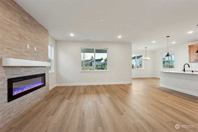 unfurnished living room with sink, a fireplace, an inviting chandelier, and light wood-type flooring