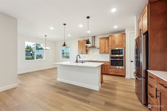 kitchen featuring a kitchen island with sink, sink, hanging light fixtures, wall chimney exhaust hood, and appliances with stainless steel finishes