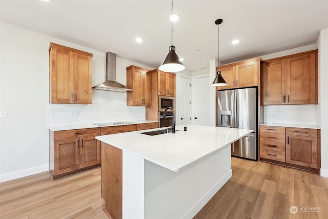 kitchen with appliances with stainless steel finishes, wall chimney exhaust hood, sink, decorative light fixtures, and an island with sink