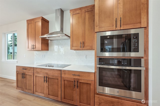 kitchen featuring built in microwave, wall chimney exhaust hood, backsplash, black electric stovetop, and light wood-type flooring