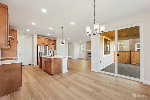 kitchen with an inviting chandelier, sink, hanging light fixtures, light wood-type flooring, and an island with sink