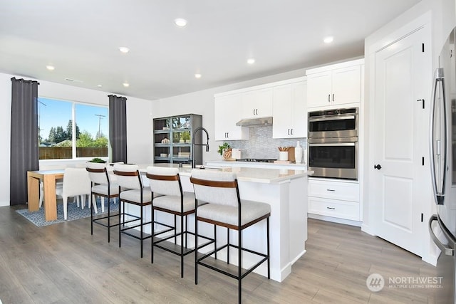 kitchen with a center island with sink, appliances with stainless steel finishes, white cabinetry, and light hardwood / wood-style floors