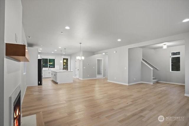 unfurnished living room with a notable chandelier and light hardwood / wood-style floors