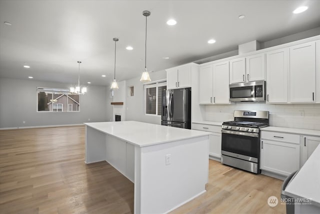 kitchen with stainless steel appliances, white cabinets, hanging light fixtures, a kitchen island, and light wood-type flooring