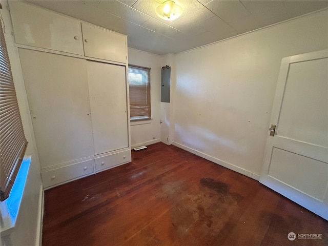 unfurnished bedroom with dark wood-type flooring, electric panel, and a closet