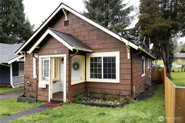 bungalow featuring roof with shingles, fence, and a front yard