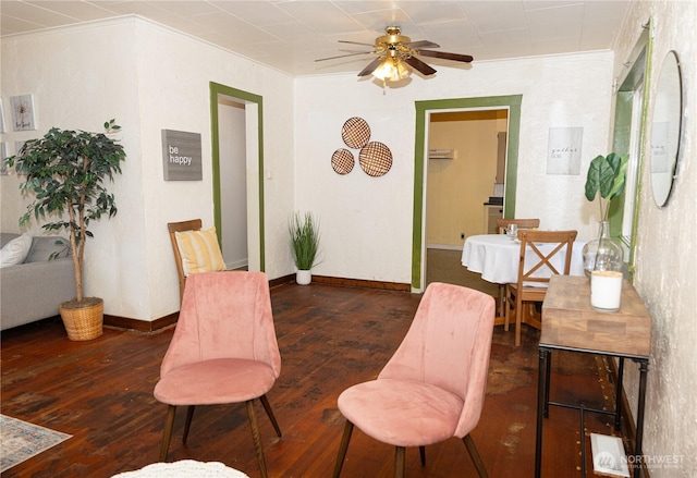 living area with baseboards, dark wood-style flooring, ceiling fan, and crown molding