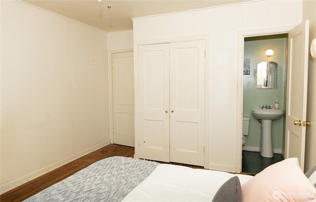 bedroom featuring a sink, ensuite bath, baseboards, dark wood-type flooring, and a closet