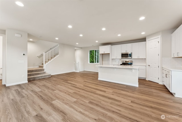 kitchen with light hardwood / wood-style floors, stainless steel appliances, a center island with sink, and white cabinets