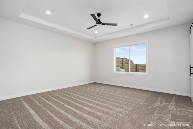 unfurnished room with carpet flooring, a barn door, a raised ceiling, and ceiling fan