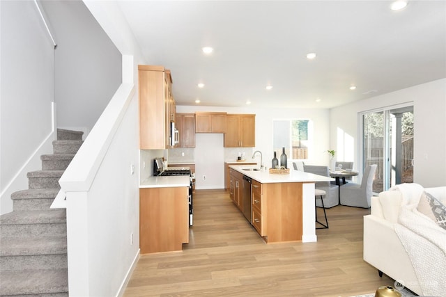 kitchen with sink, stainless steel appliances, backsplash, light hardwood / wood-style floors, and a center island with sink