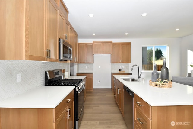 kitchen with a kitchen island with sink, sink, light wood-type flooring, tasteful backsplash, and stainless steel appliances