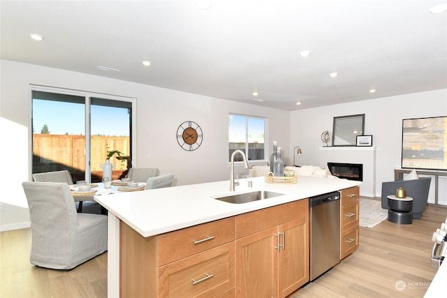 kitchen featuring stainless steel dishwasher, sink, a kitchen island with sink, and light hardwood / wood-style flooring