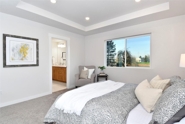 bedroom with light carpet, ensuite bathroom, and a raised ceiling