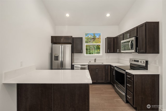 kitchen with hardwood / wood-style floors, sink, vaulted ceiling, dark brown cabinetry, and stainless steel appliances