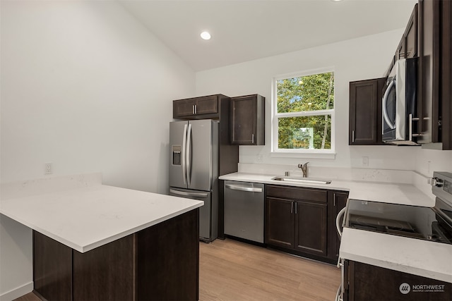 kitchen with a peninsula, light wood-style flooring, a sink, dark brown cabinetry, and appliances with stainless steel finishes