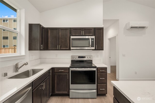 kitchen with sink, a wall mounted AC, lofted ceiling, appliances with stainless steel finishes, and light wood-type flooring