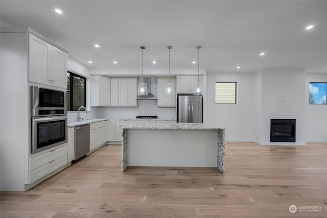 kitchen featuring white cabinetry, a center island, pendant lighting, stainless steel appliances, and wall chimney range hood