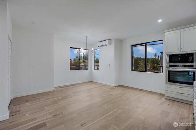 unfurnished living room with a wall mounted air conditioner, a wealth of natural light, and light hardwood / wood-style floors