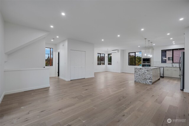 unfurnished living room featuring sink, light hardwood / wood-style flooring, and a wall mounted AC