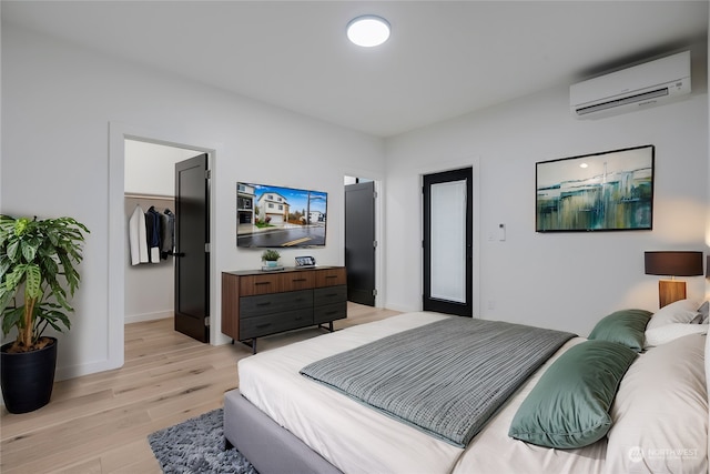 bedroom featuring a spacious closet, light hardwood / wood-style floors, and an AC wall unit