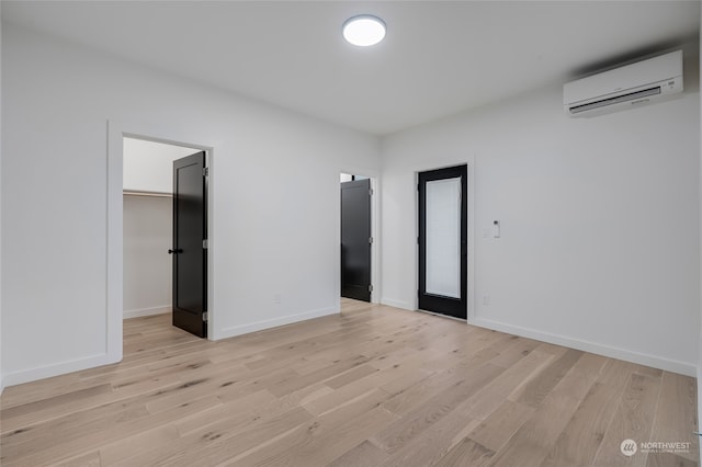 unfurnished bedroom featuring a walk in closet, a wall mounted AC, and light hardwood / wood-style flooring