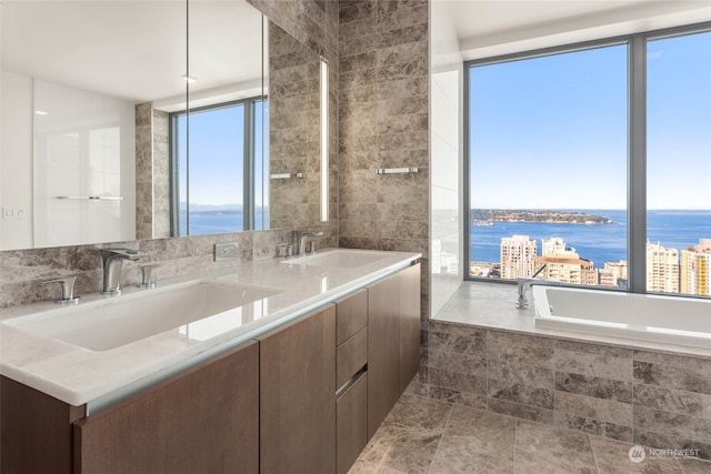 bathroom with vanity, a water view, tile patterned floors, and tiled tub